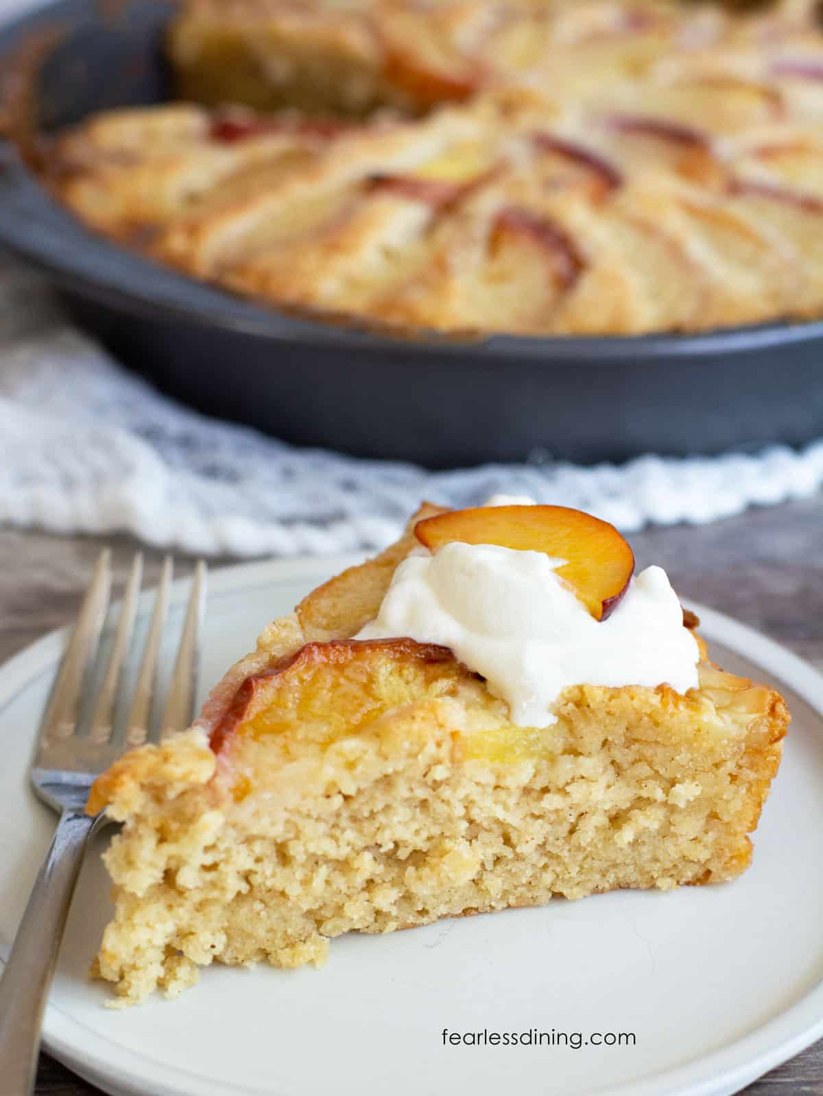 A slice of peach kuchen on a plate. It is topped with some fresh whipped cream.