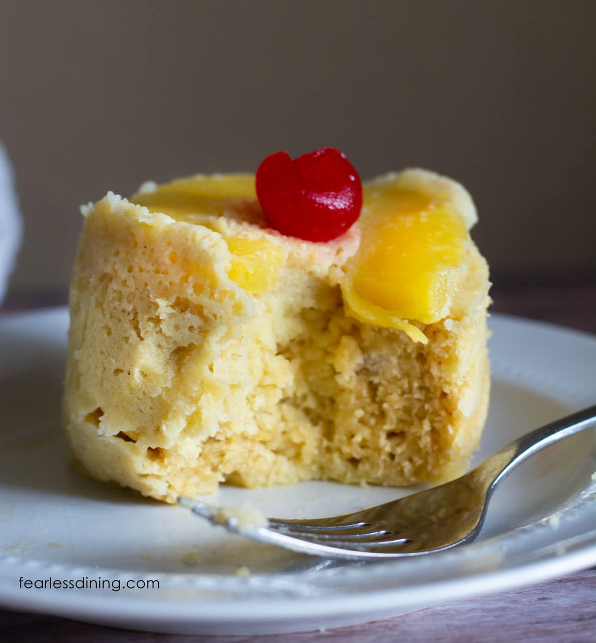 A pineapple upside down mug cake on a plate with a piece cut out.