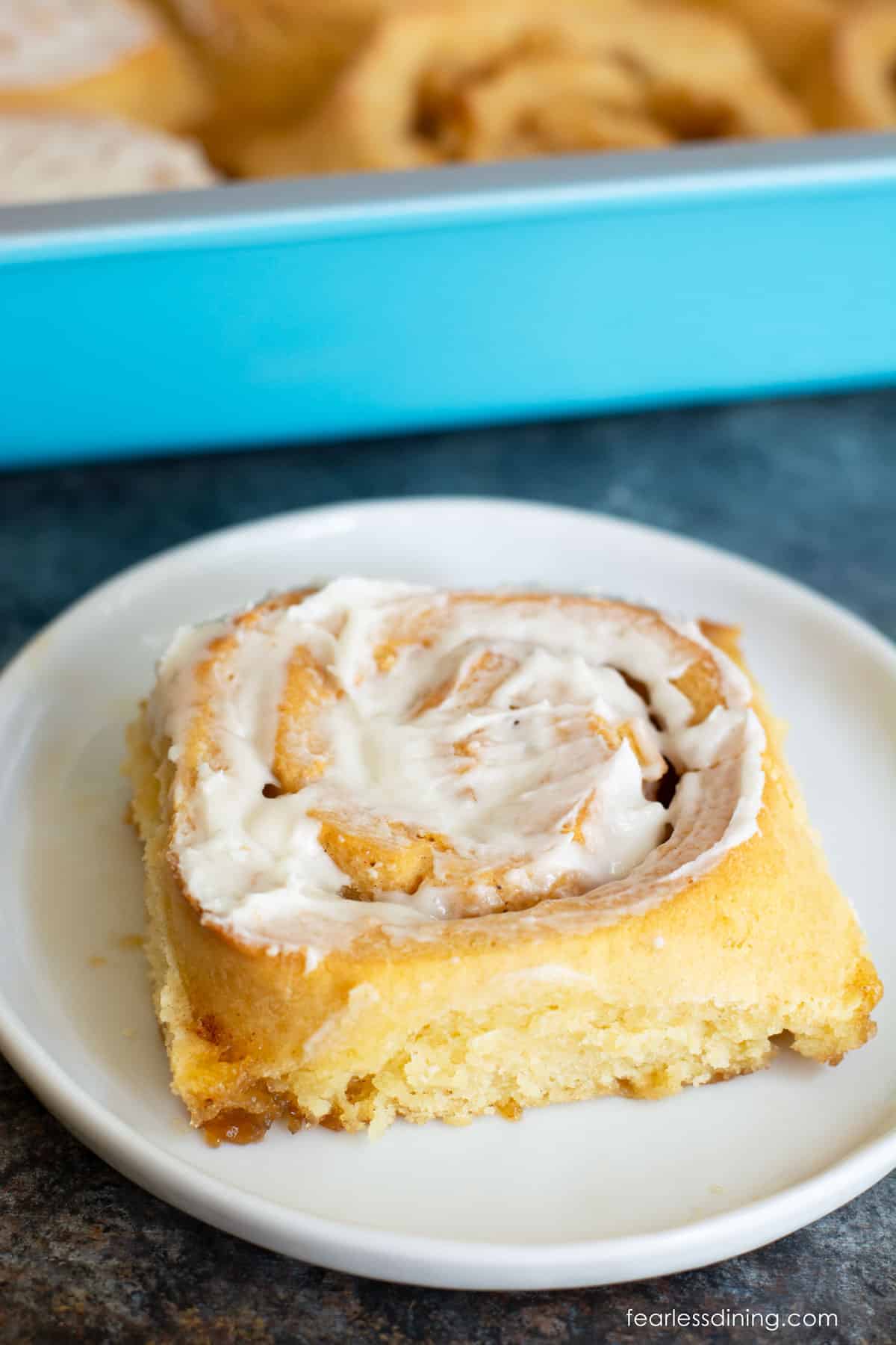 A frosted gluten free apple cinnamon roll on a white plate.