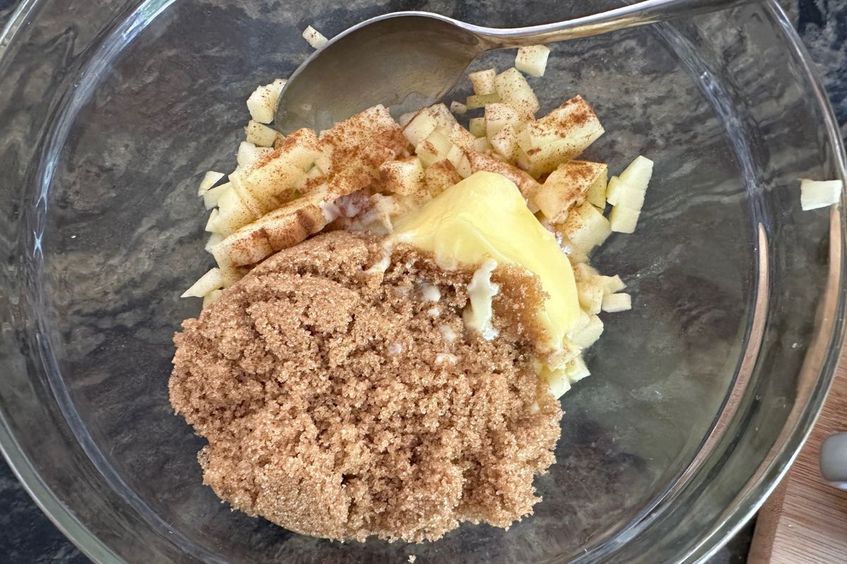 A bowl with melted butter, dices apples, brown sugar, and cinnamon.