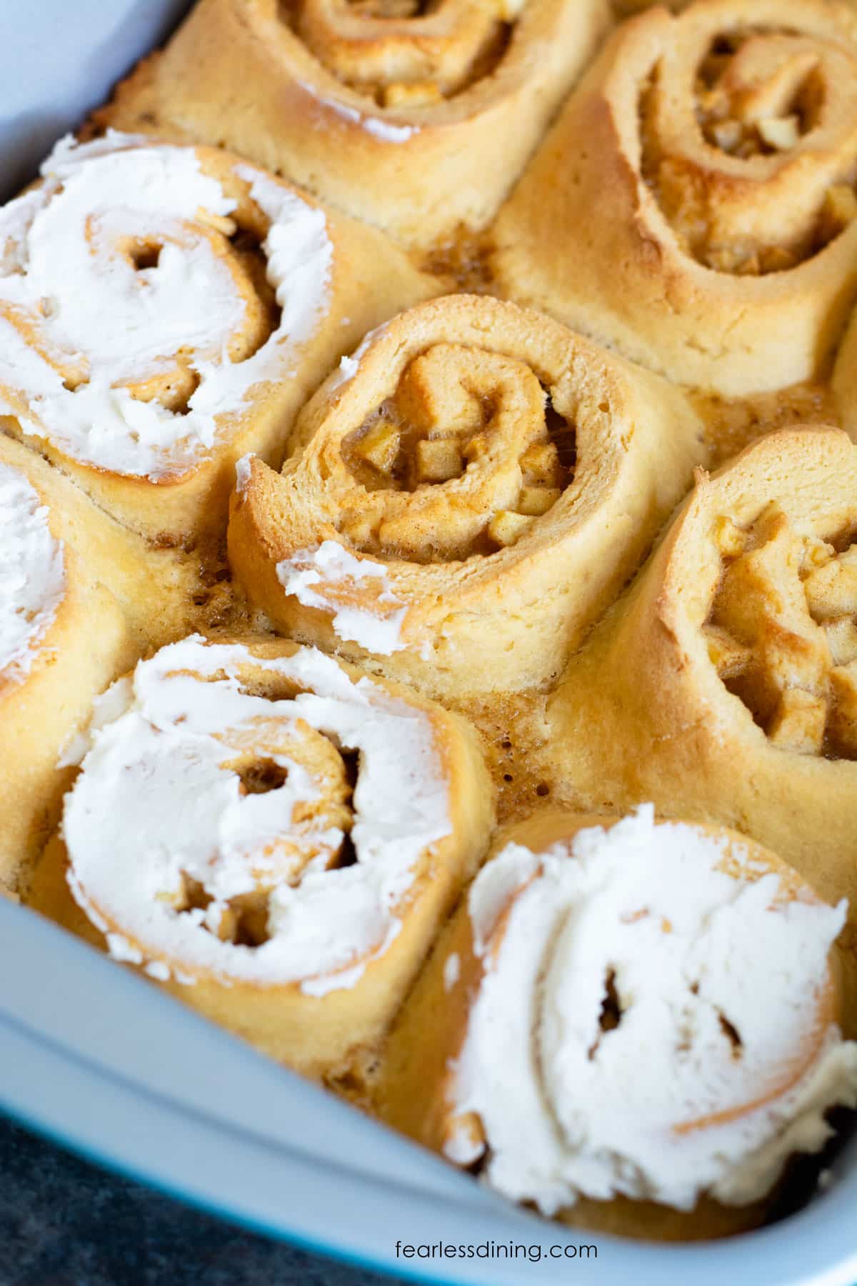 A baking pan filled with apple cinnamon rolls. Three are frosted.