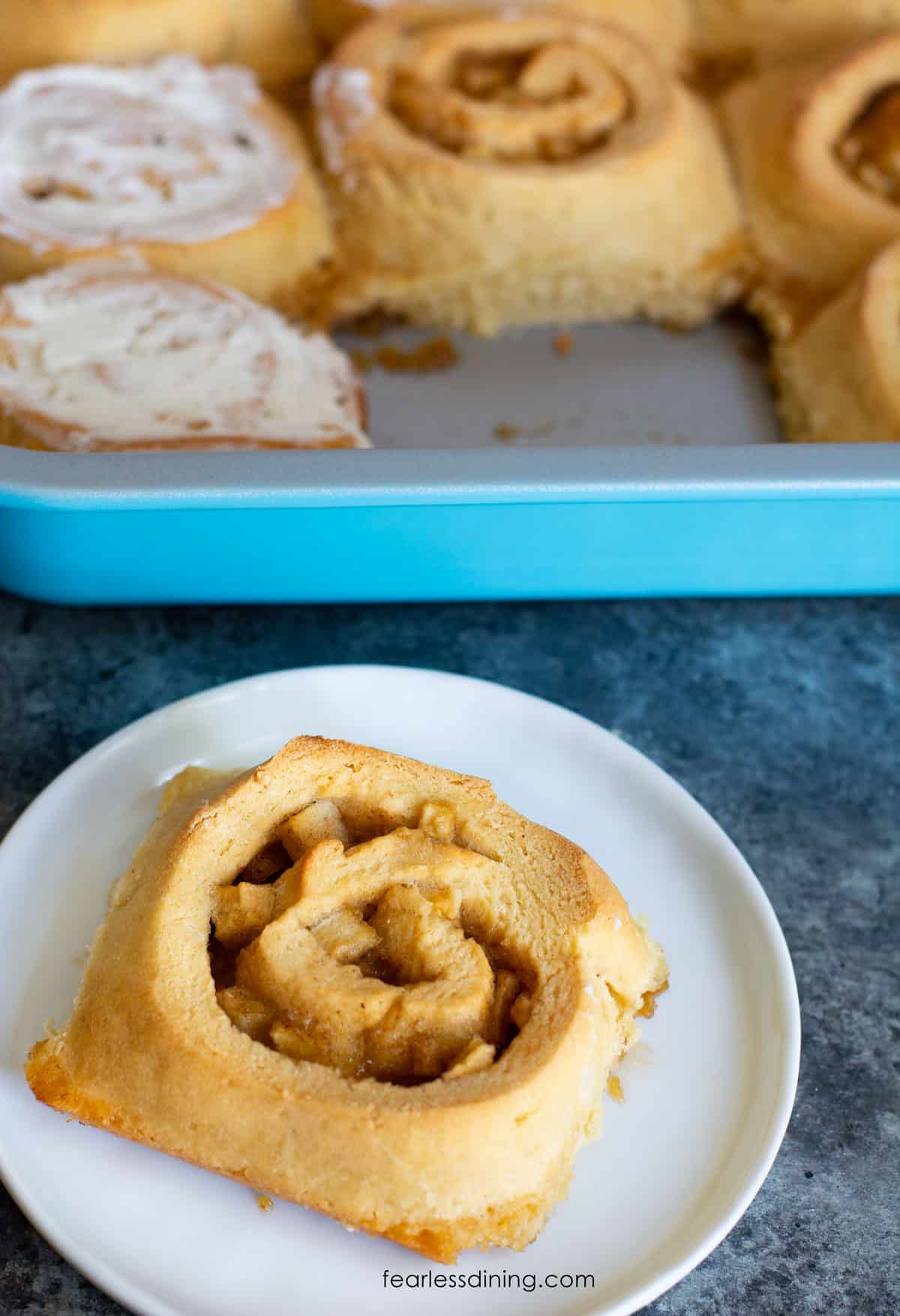 An apple cinnamon roll on a small white plate.