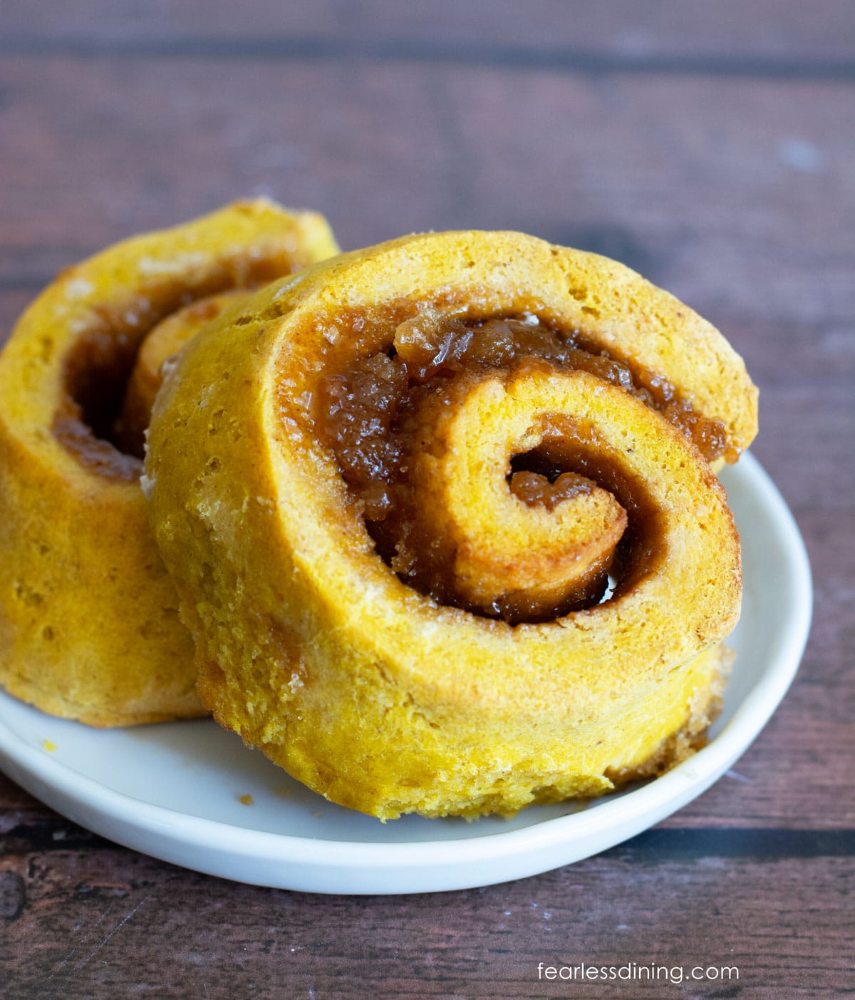 Two gluten free pumpkin cinnamon rolls on a plate. They are not iced.