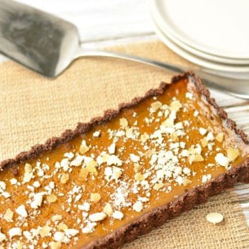 A whole pumpkin tart on a table next to plates and a serving spoon.