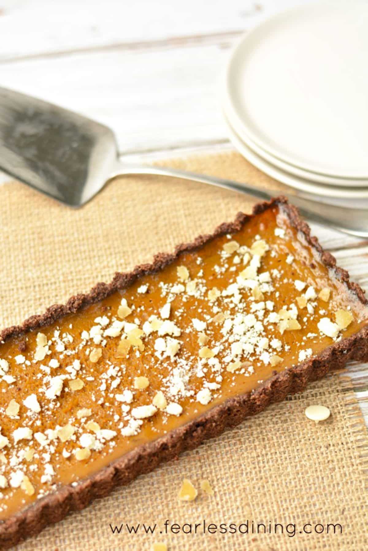 A whole pumpkin tart on a table next to plates and a serving spoon.