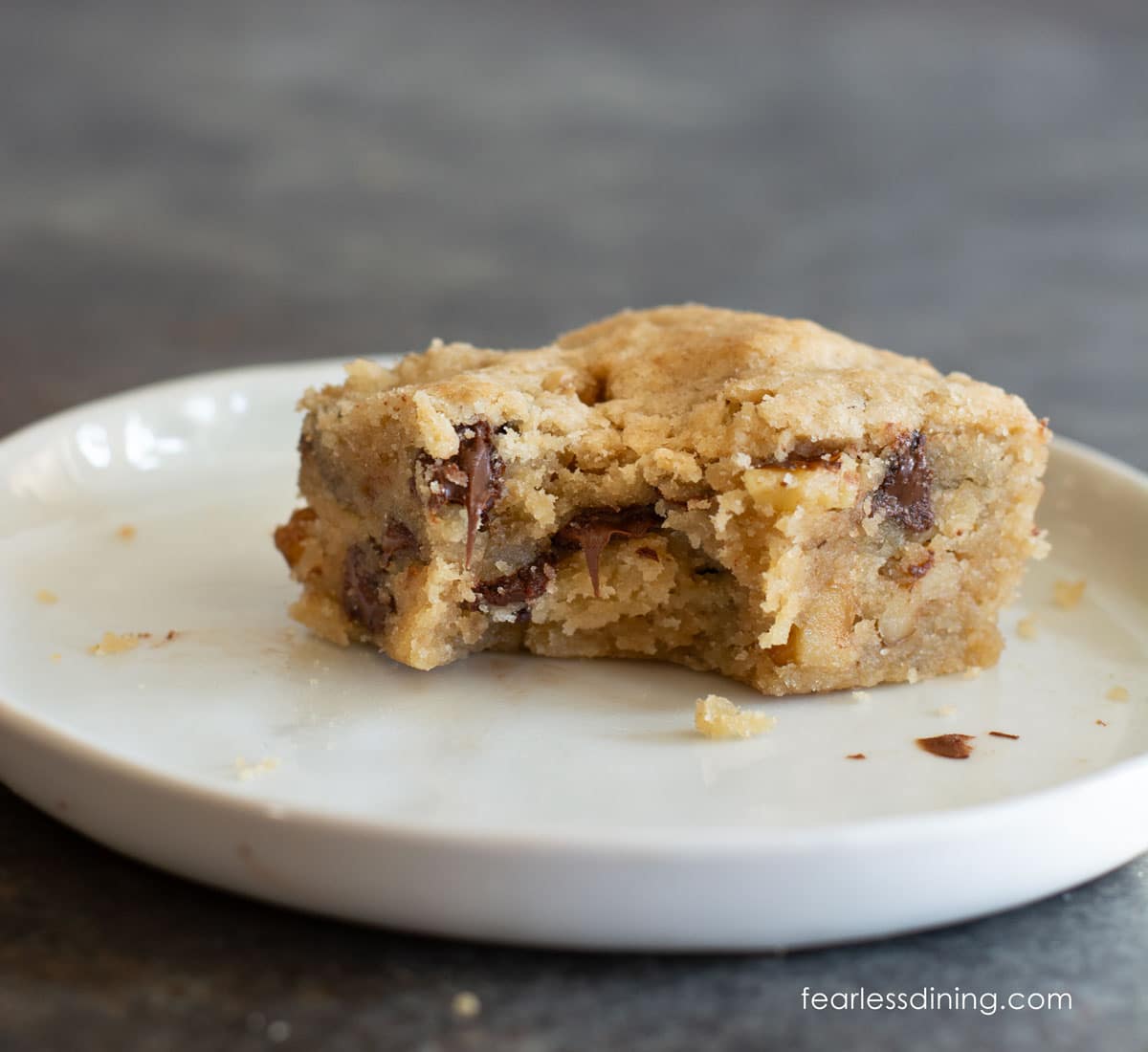 A gluten free maple walnut bar on a small white plate. A bite is taken out of the bar.