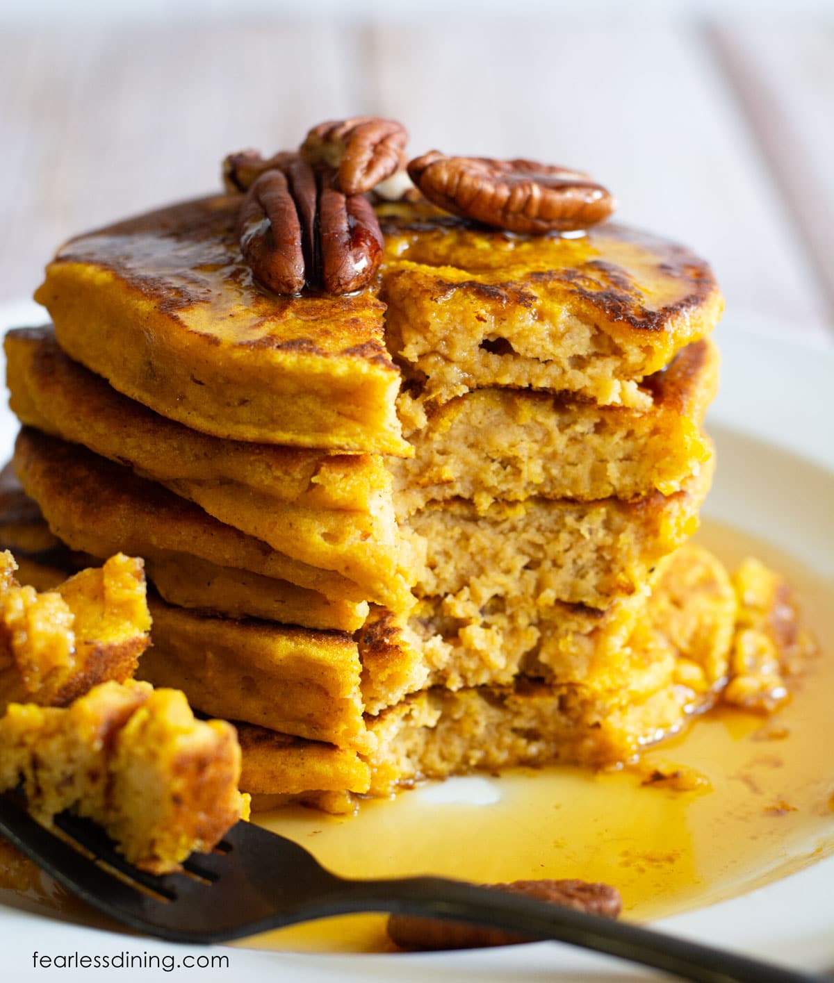 A stack of gluten free pumpkin pancakes with a bite cut out.