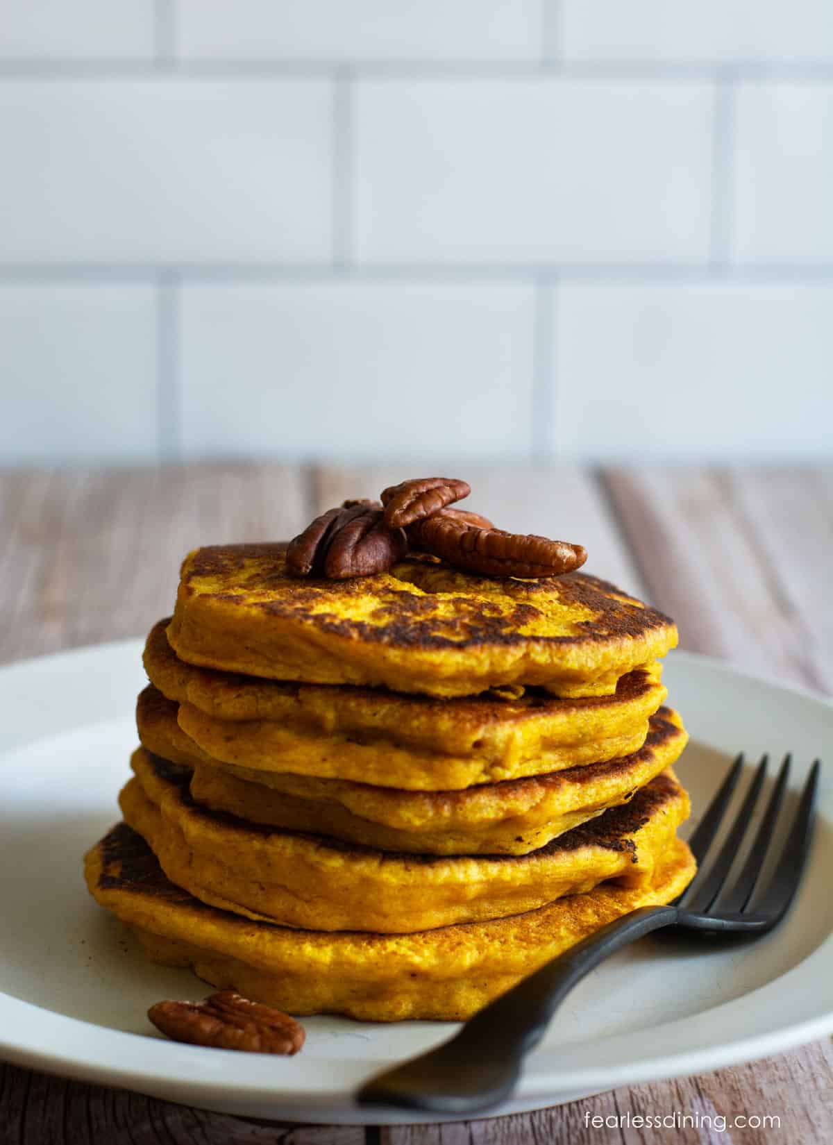 A stack of pumpkin pancakes topped with pecan halves.