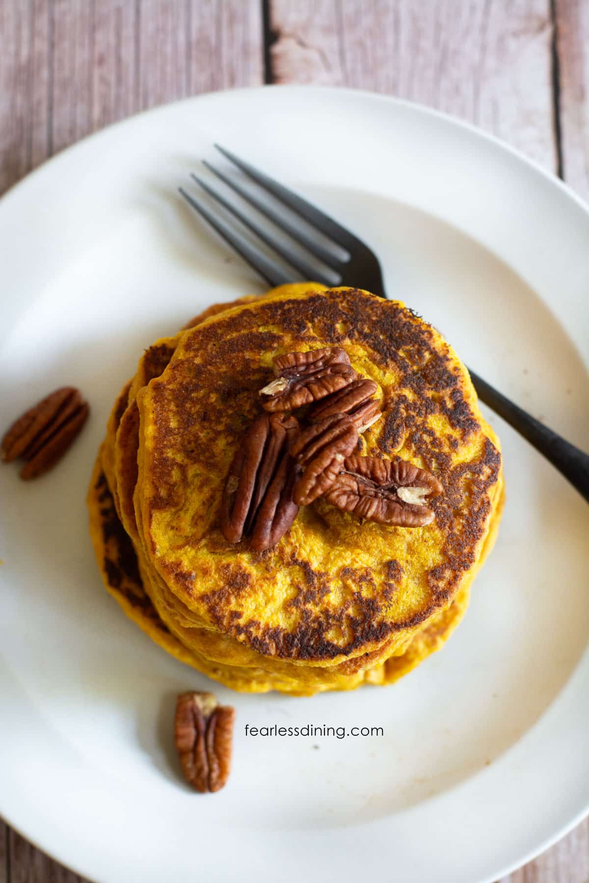 The top view of a stack of pumpkin pancakes topped with raw pecans.