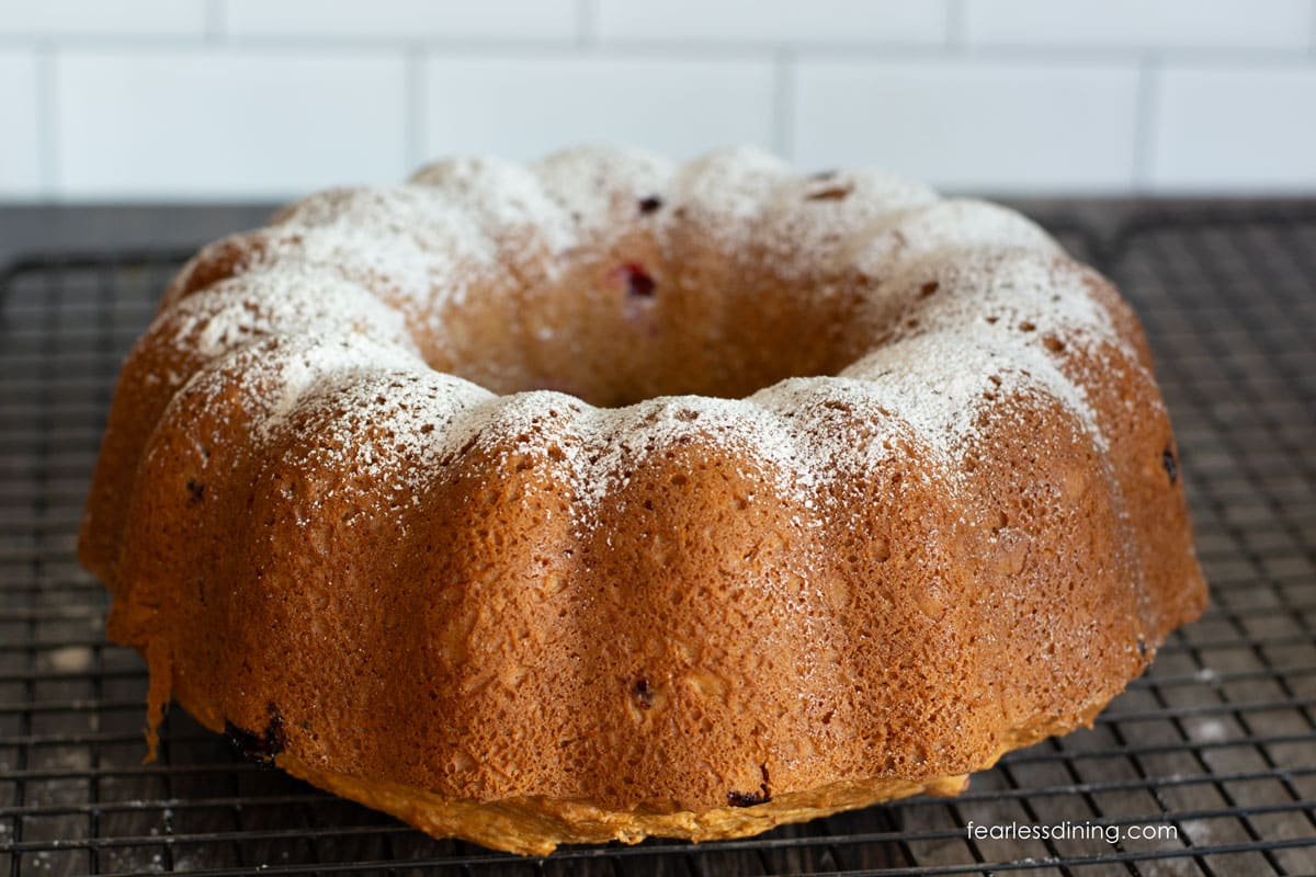 A picture of the cranberry bundt cake on a cooling rack. The cake is dusted with powdered sugar.
