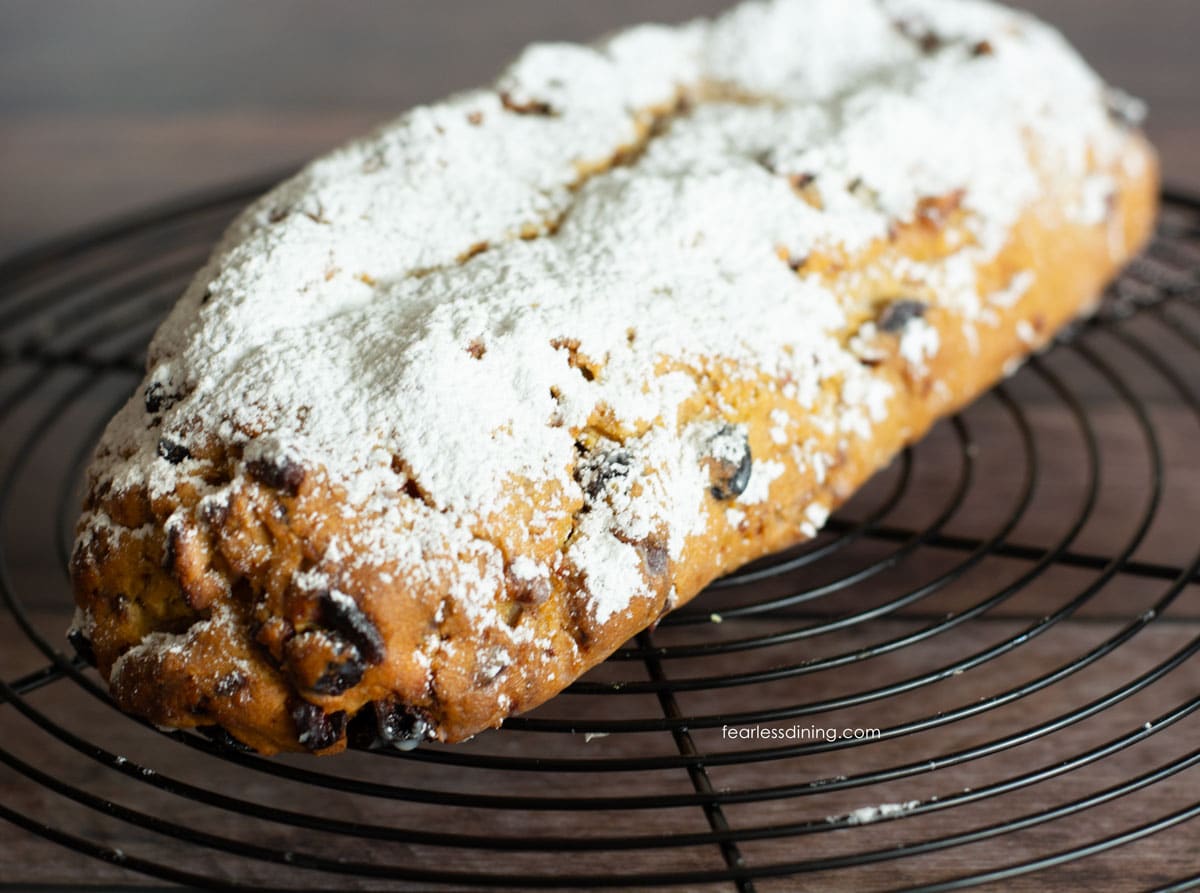 A loaf of stollen on a cooling rack with powdered sugar dusted over the top and sides.