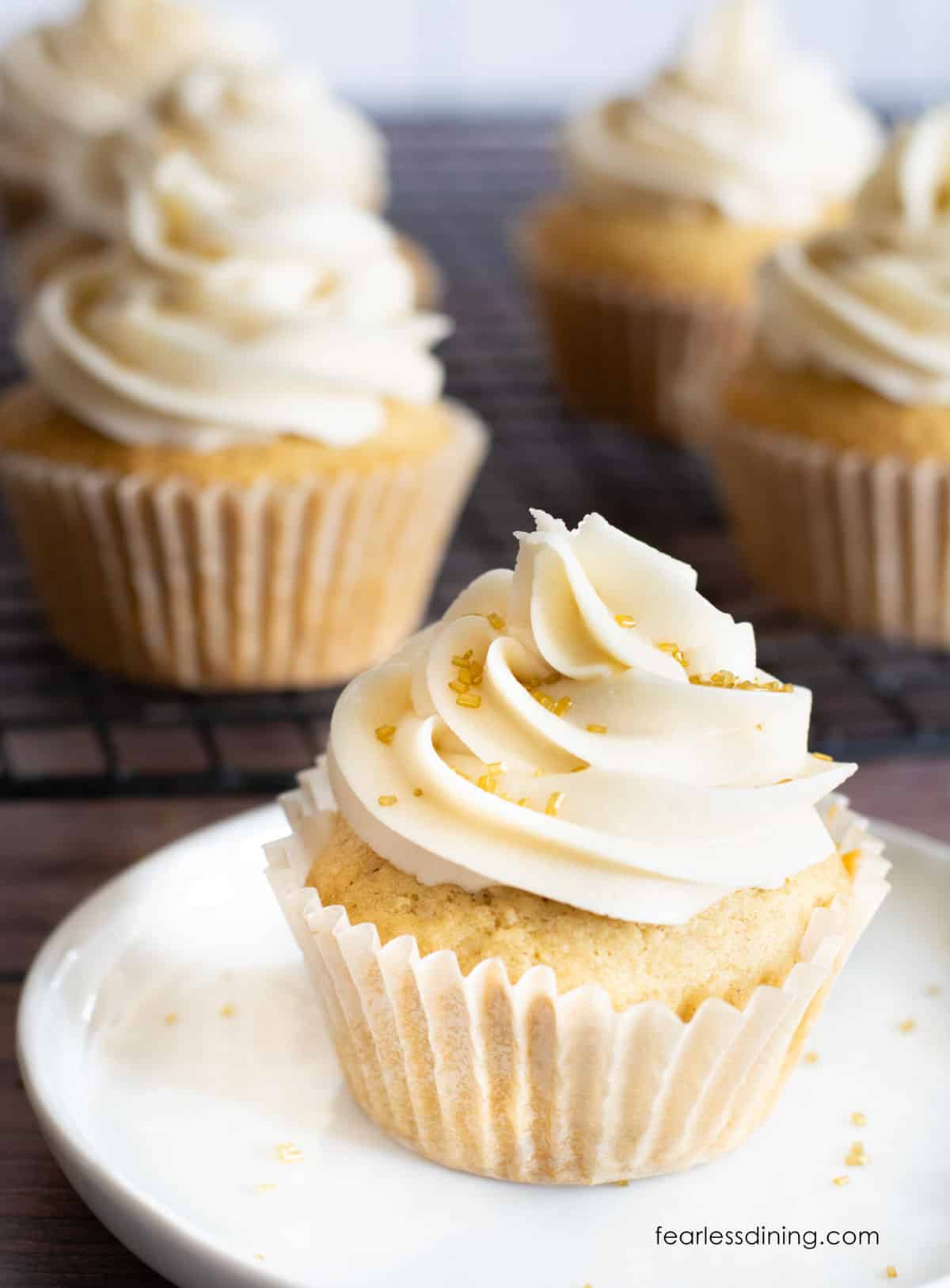 Lots of frosted gluten free eggnog cupcakes. They are topped with gold sprinkles.