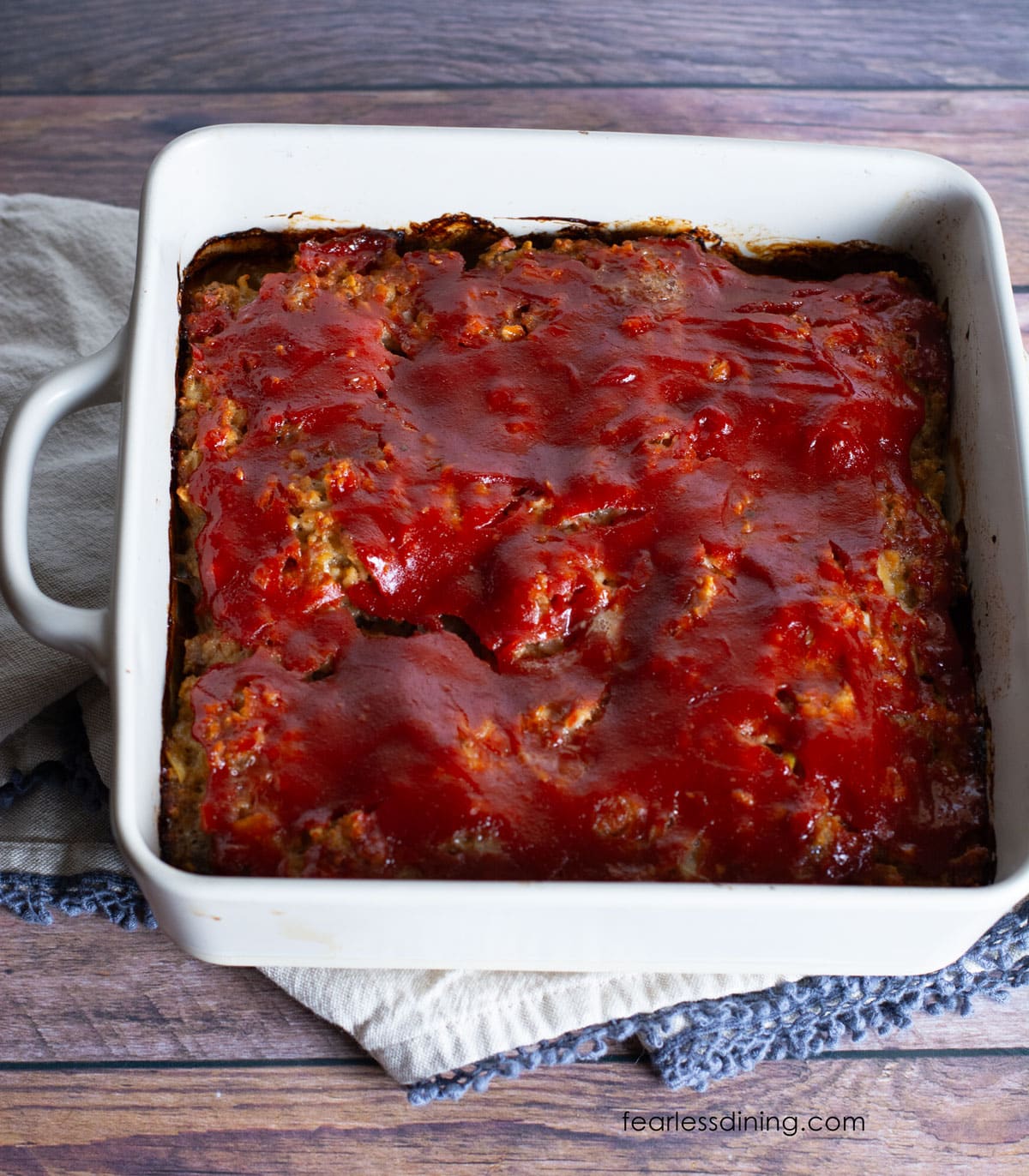 A baked gluten free meatloaf with a ketchup glaze in a white casserole dish.