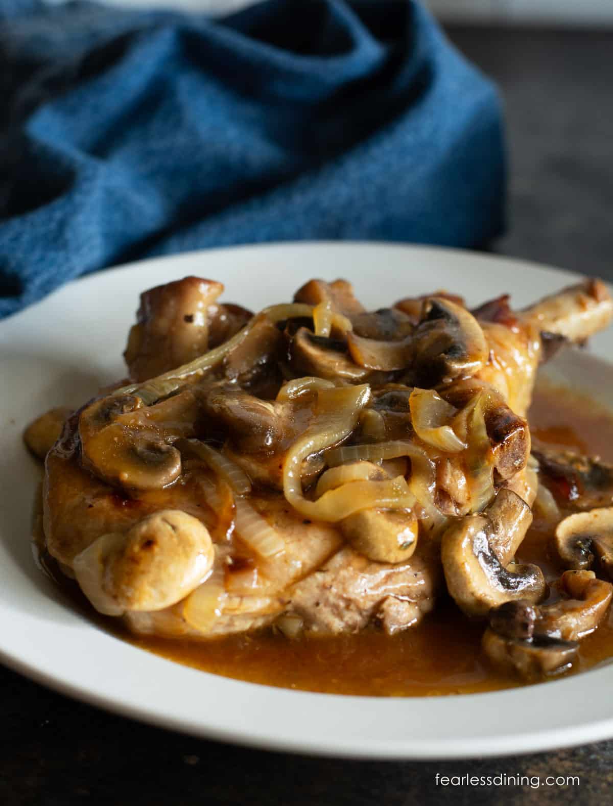 A large bone-in pork chop topped with caramelized onions and mushrooms on a white plate.
