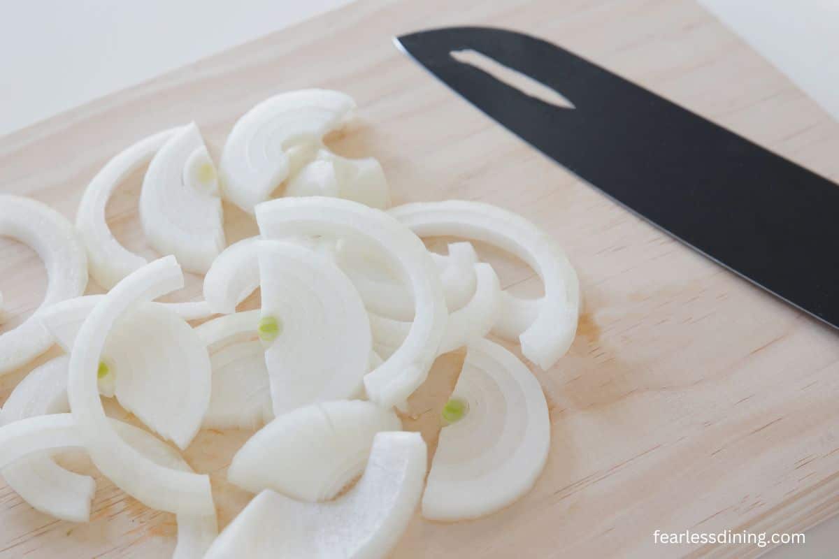 Sliced onions on a small wooden cutting board.