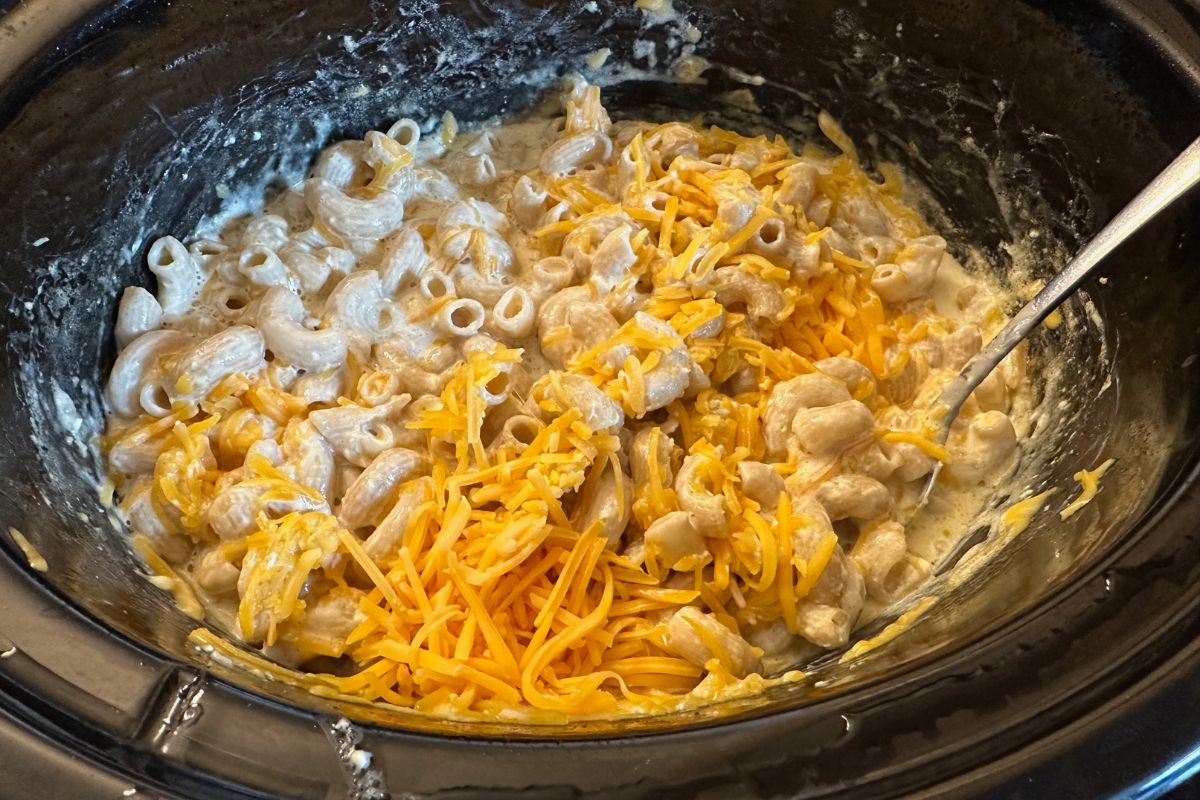 Adding the shredded cheese to the partially cooked macaroni.