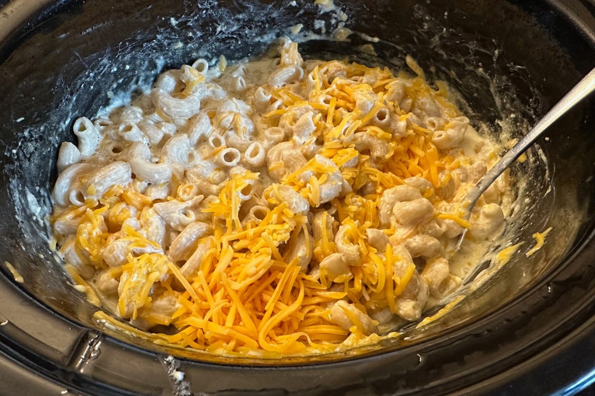 Adding the shredded cheese to the partially cooked macaroni.