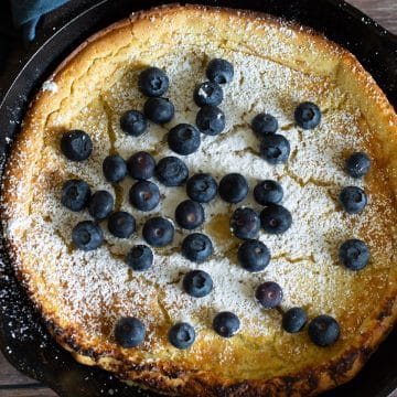 A top view of the gluten free Dutch baby pancake. It is dusted in powdered sugar and topped with blueberries.