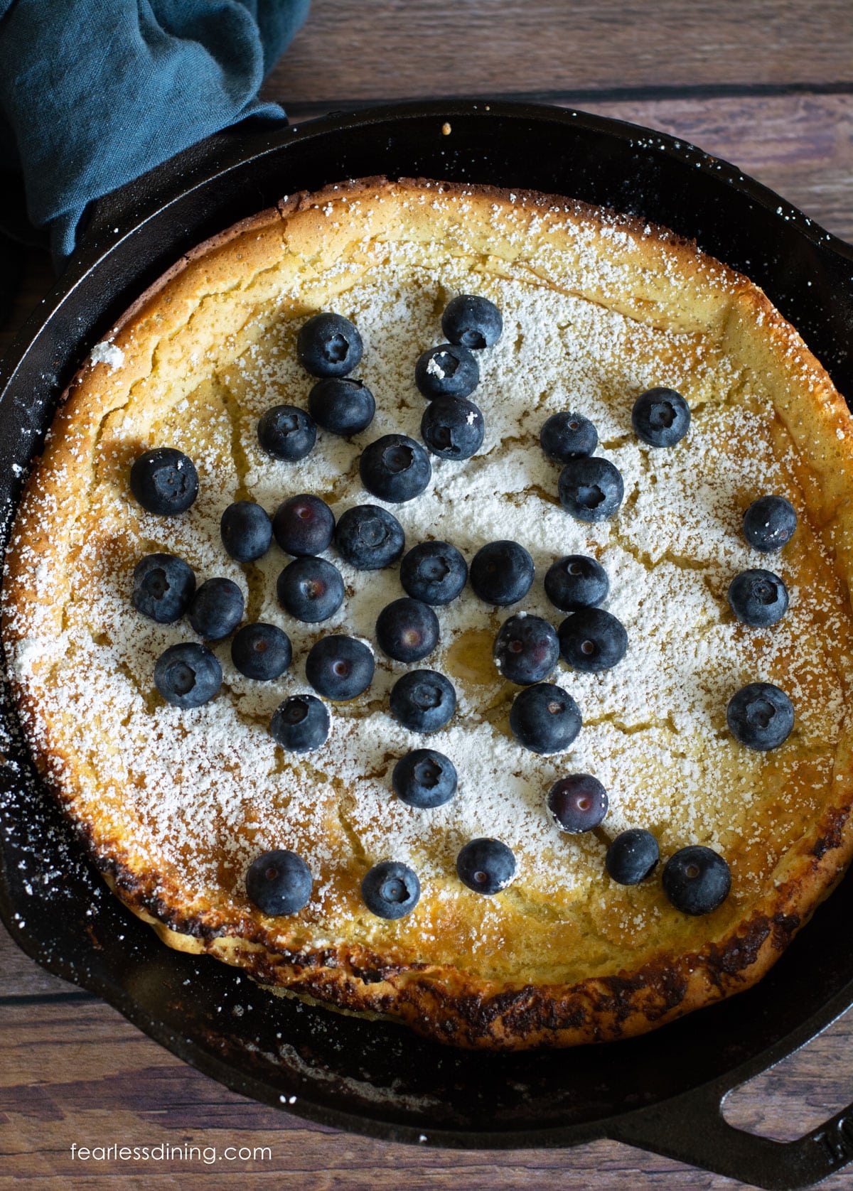 A top view of the gluten free Dutch baby pancake. It is dusted in powdered sugar and topped with blueberries.