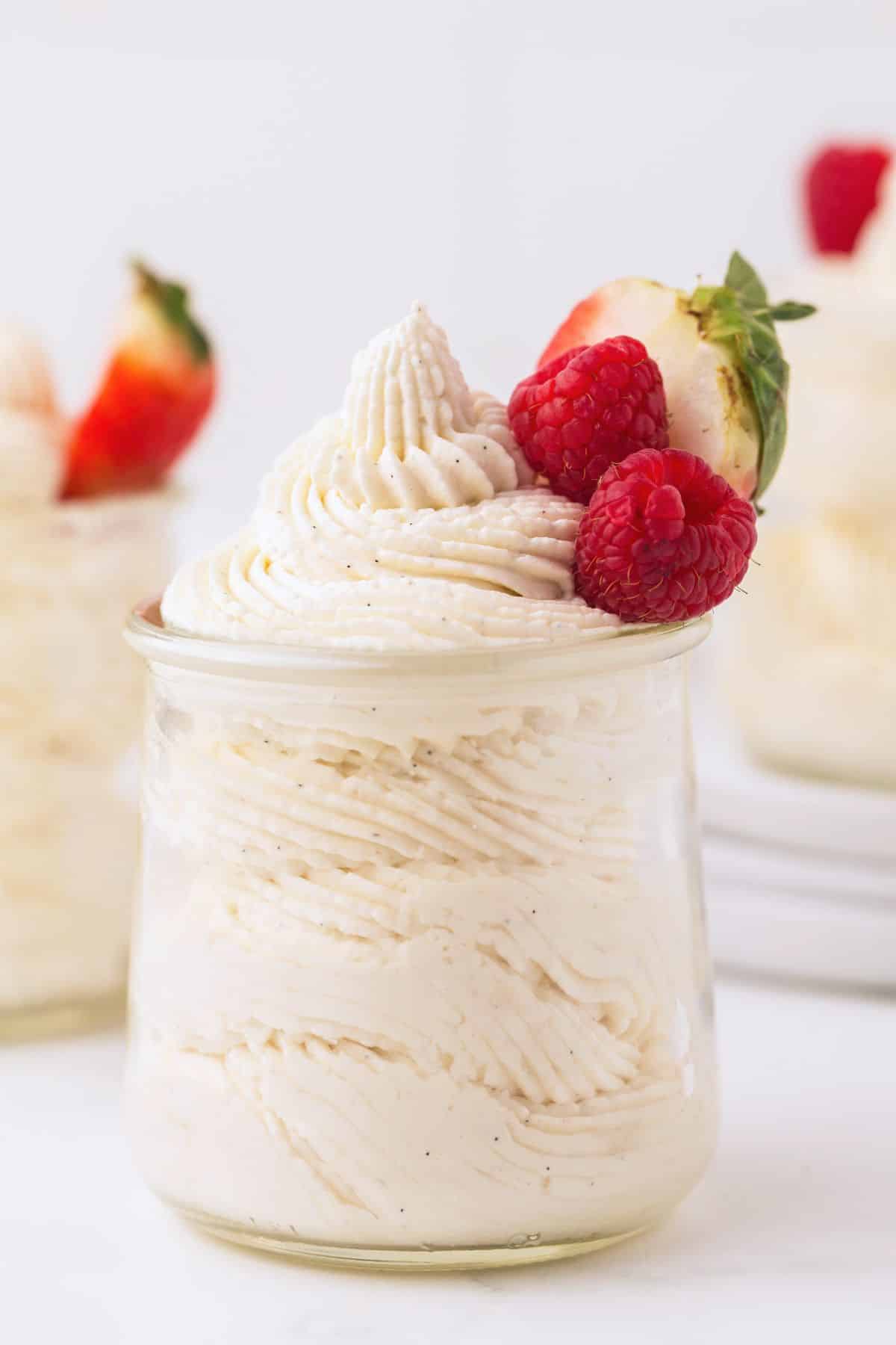 Three small glass jars filled with vanilla bean mousse. They are garnished with fresh berries.