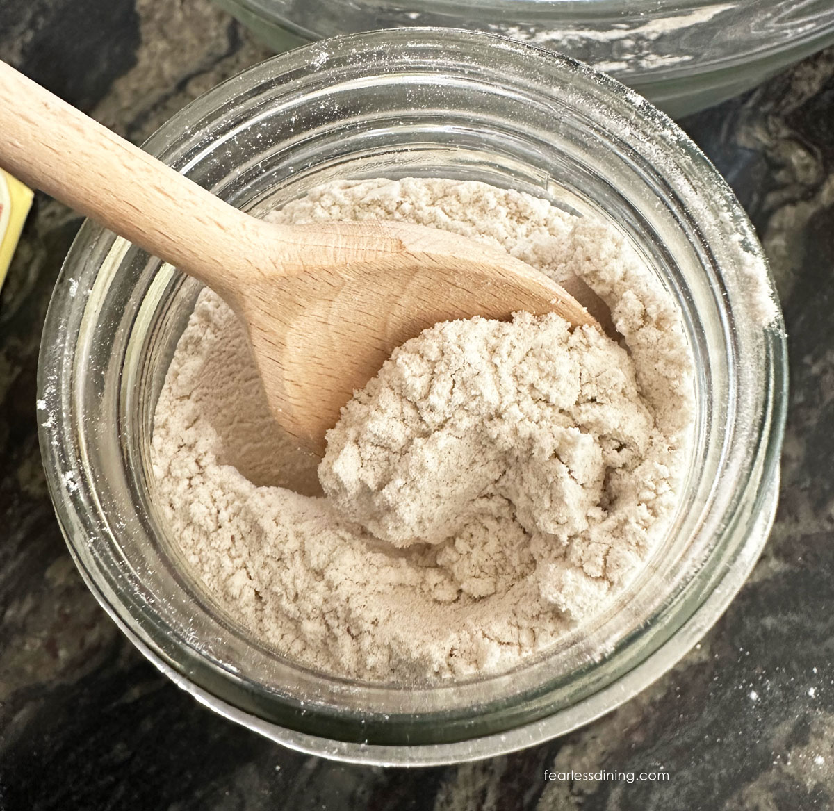 The top view of a jar filled with my homemade gluten free whole grain flour blend. There is a wooden spoon in the jar.