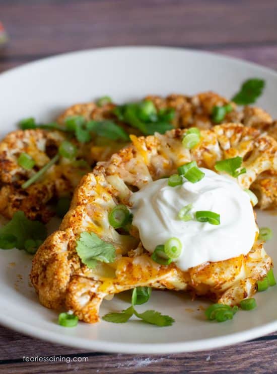 Two air fryer cauliflower steaks on a plate. They are garnished with sour cream and scallions.