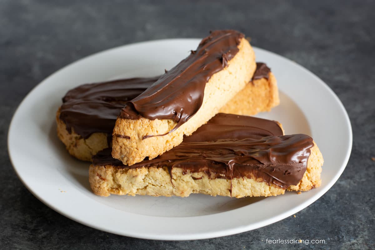 A white plate with four chocolate dipped almond biscotti.