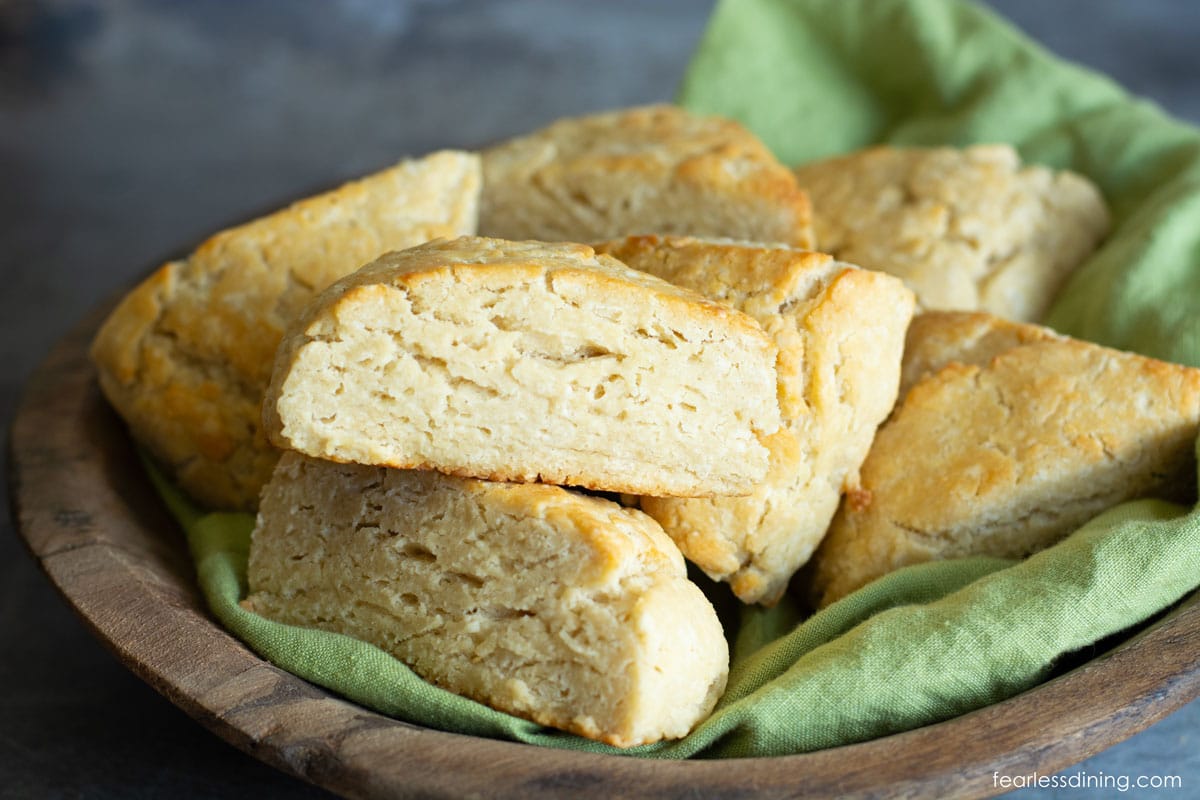 A wooden bowl with a green napkin nand eight gluten free buttermilk scones.