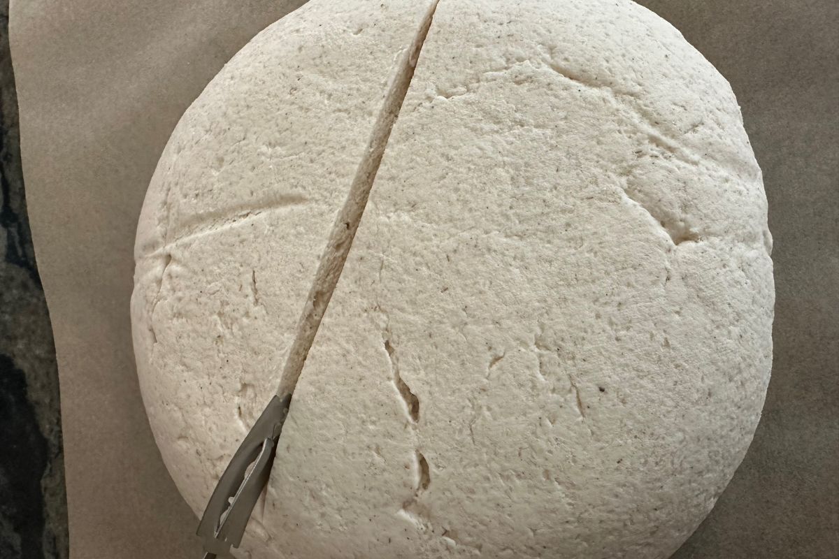 Using a bread lame to make a half inch deep slash on the top of the bread dough ball.