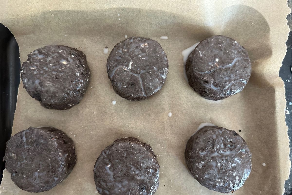 Six chocolate biscuits brushed with buttermilk, ready to bake.
