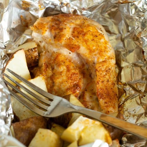 A seasoned chicken breast and potatoes cooked in an air fryer foil packet.