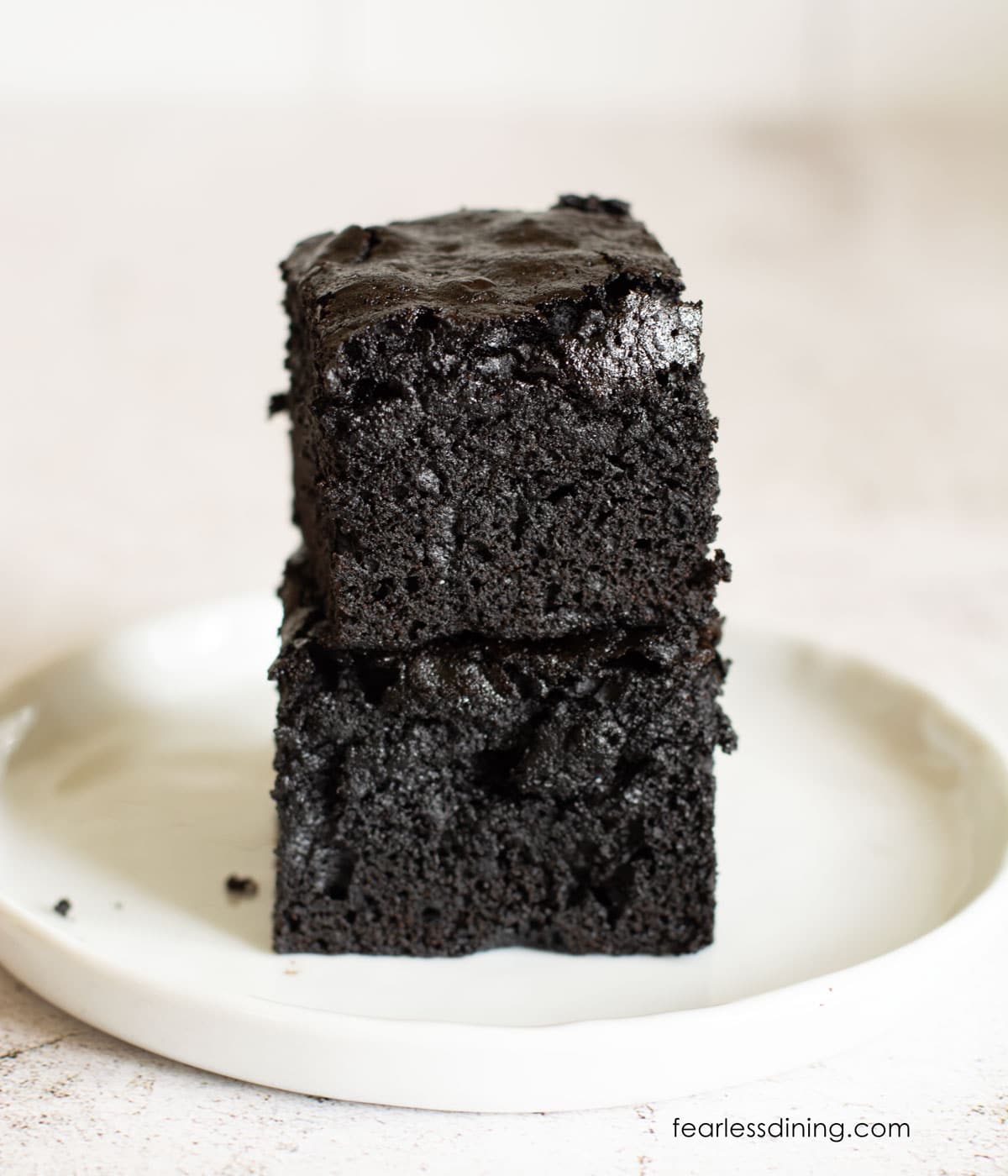 A stack of two fudgy brownies on a small white plate.