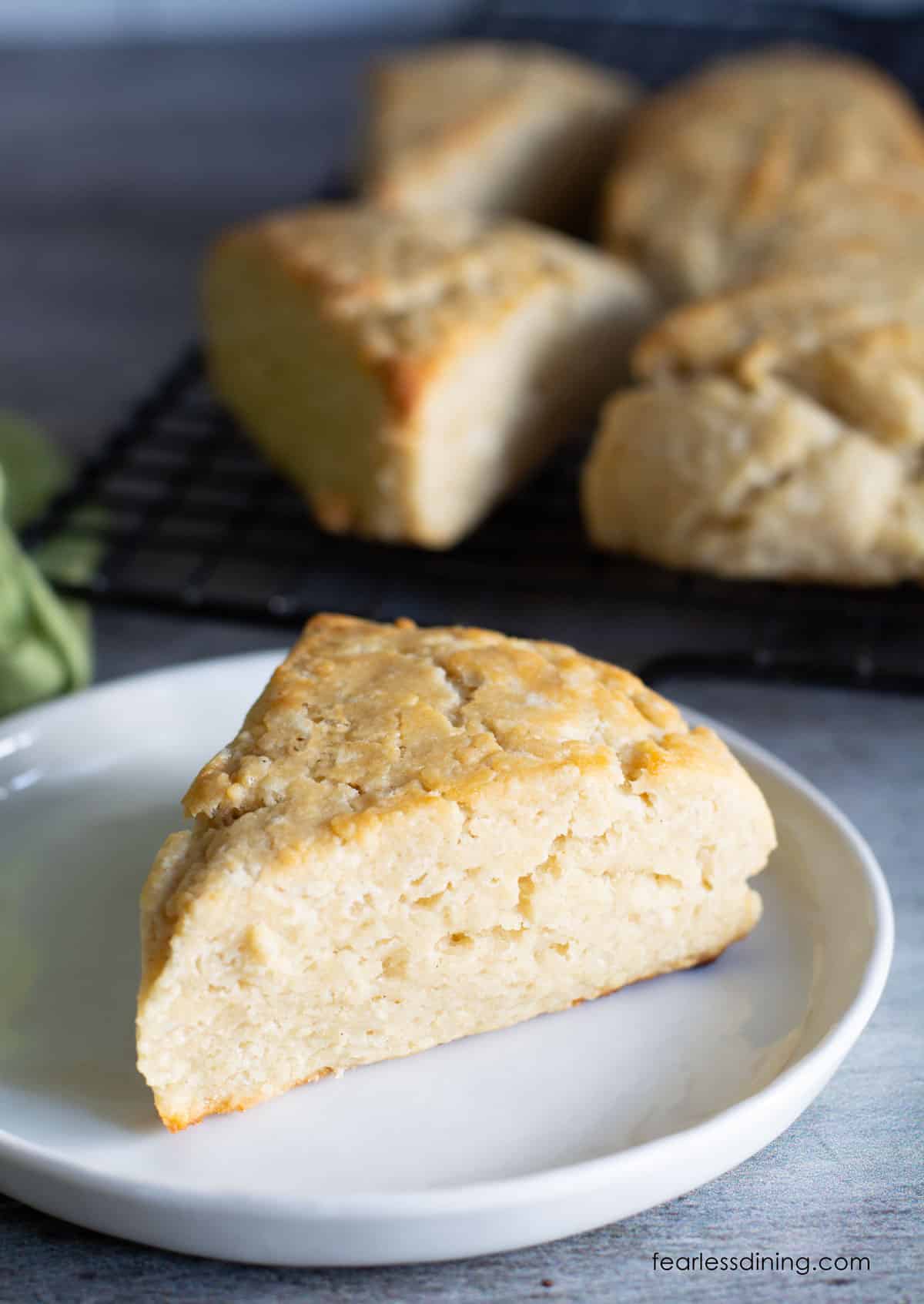 A scone on a white plate next to the rack of scones.