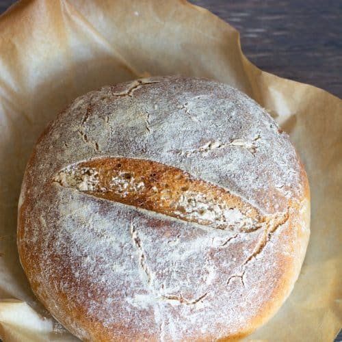 A baked sourdough boule fresh out of the oven. It is on a piece of parchment paper.