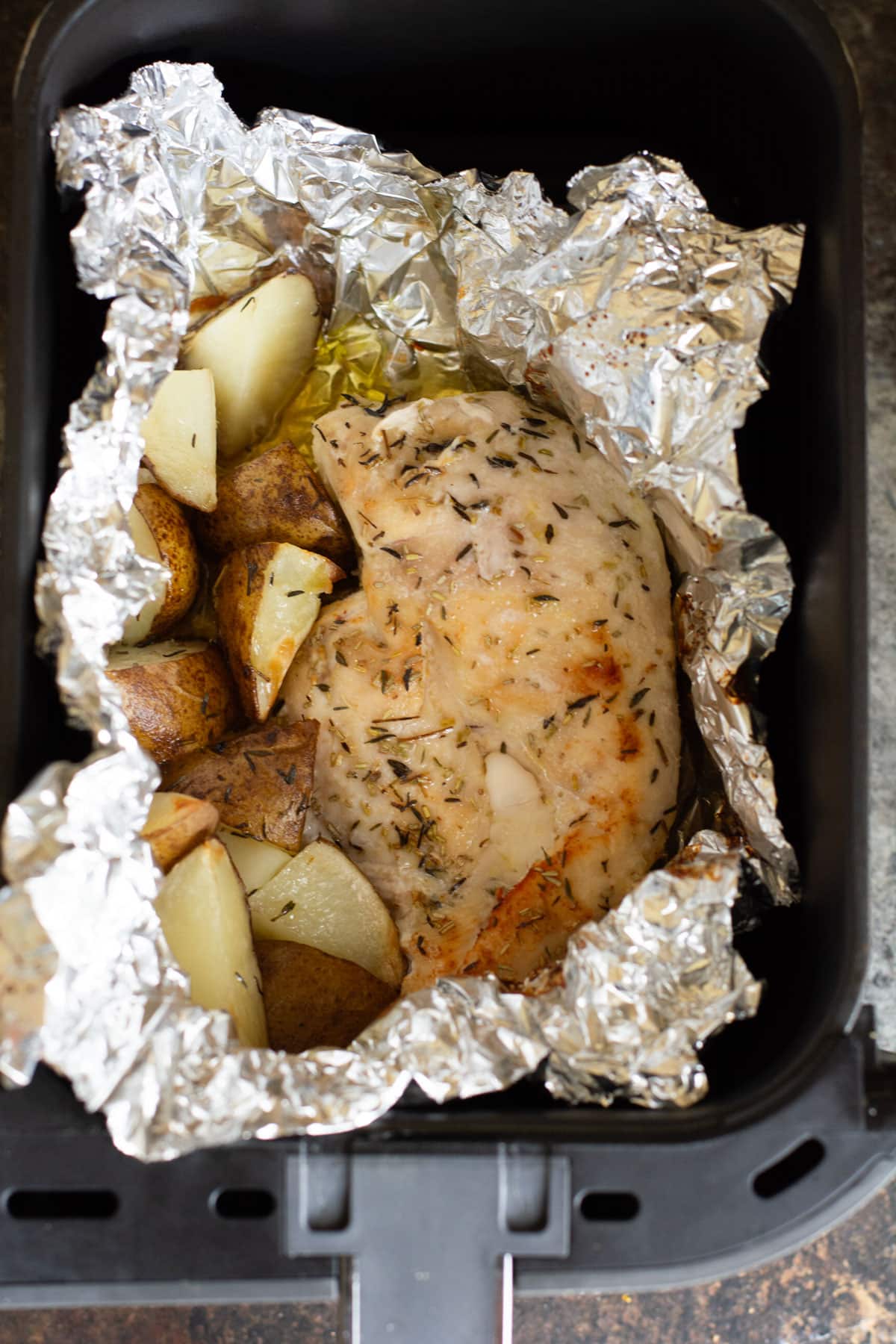 An herb coated cooked chicken breast in a foil packet.