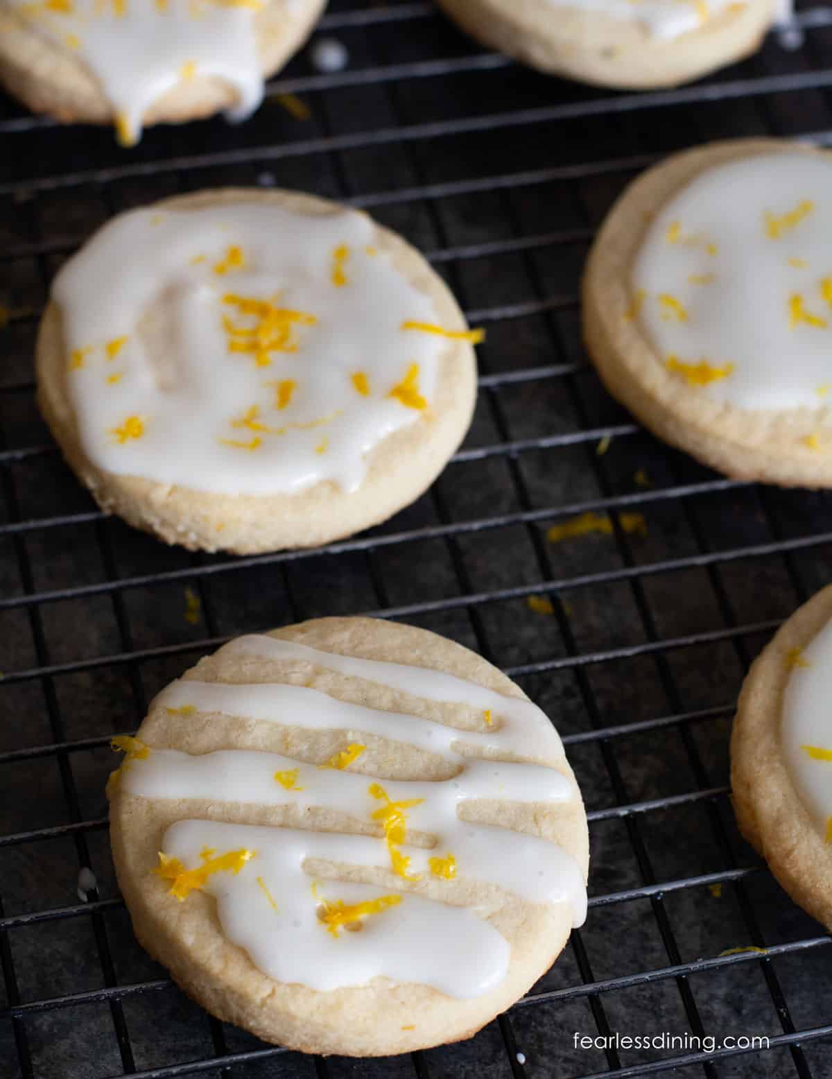 Lemon shortbread cookies on a rack. They have an icing drizzle and lemon zest on top.