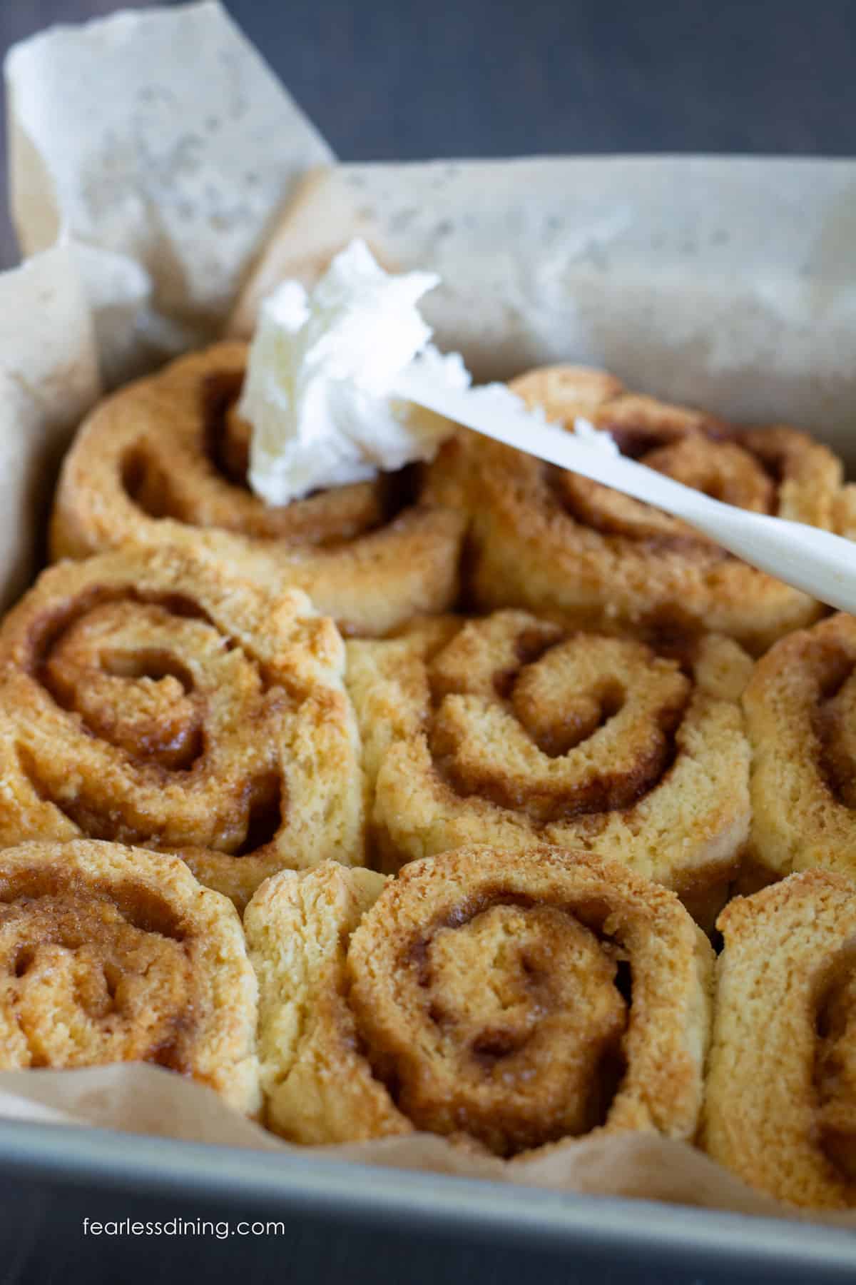 Spreading the frosting over the cinnamon rolls.