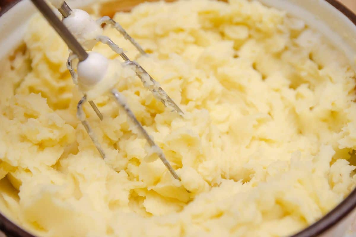 Using an electric mixer to whip the potatoes.