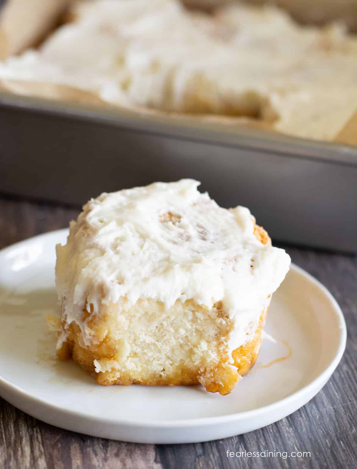 A fluffy, frosted gluten free yeast free cinnamon roll on a small white plate.