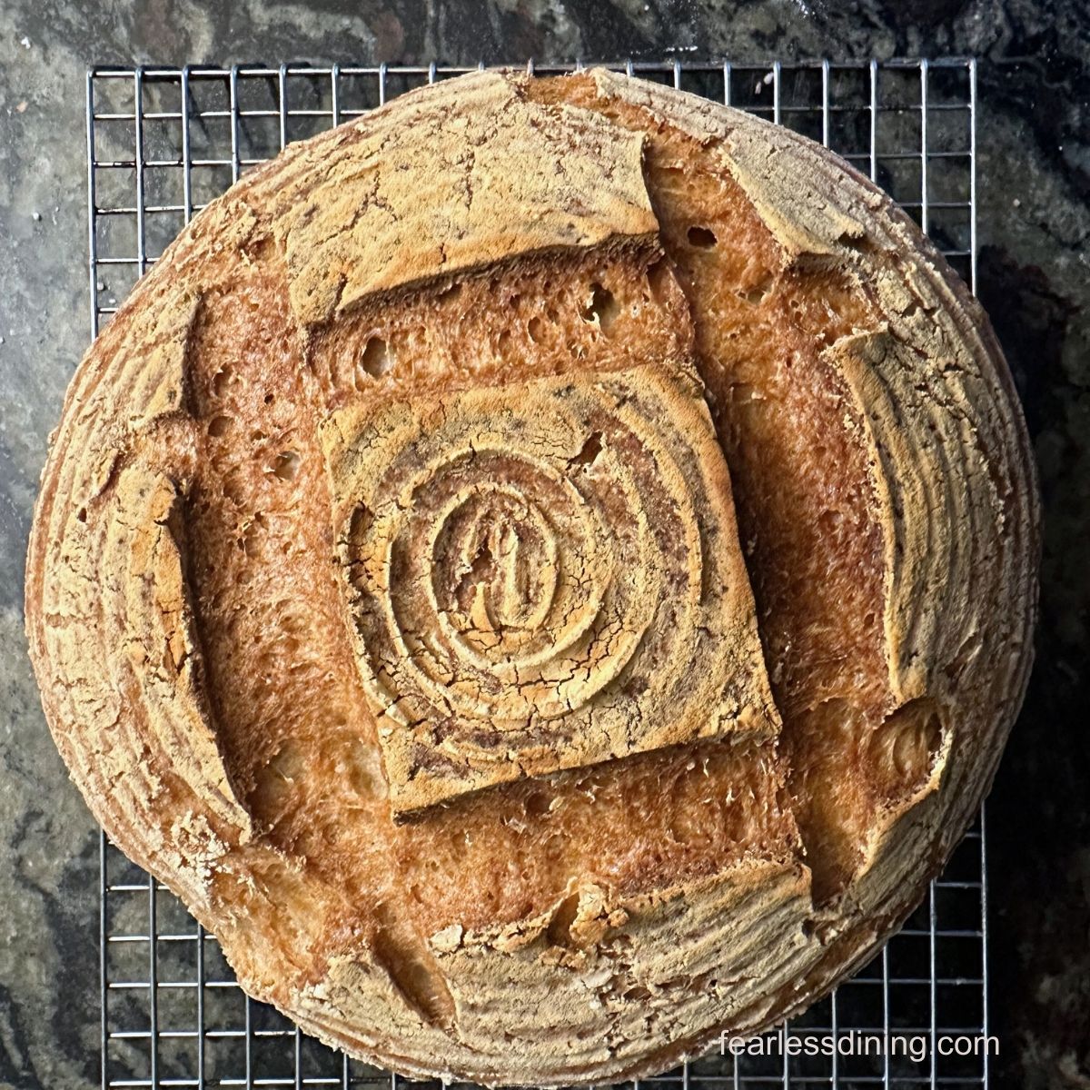 A baked gluten free sourdough boule on a wire cooling rack.