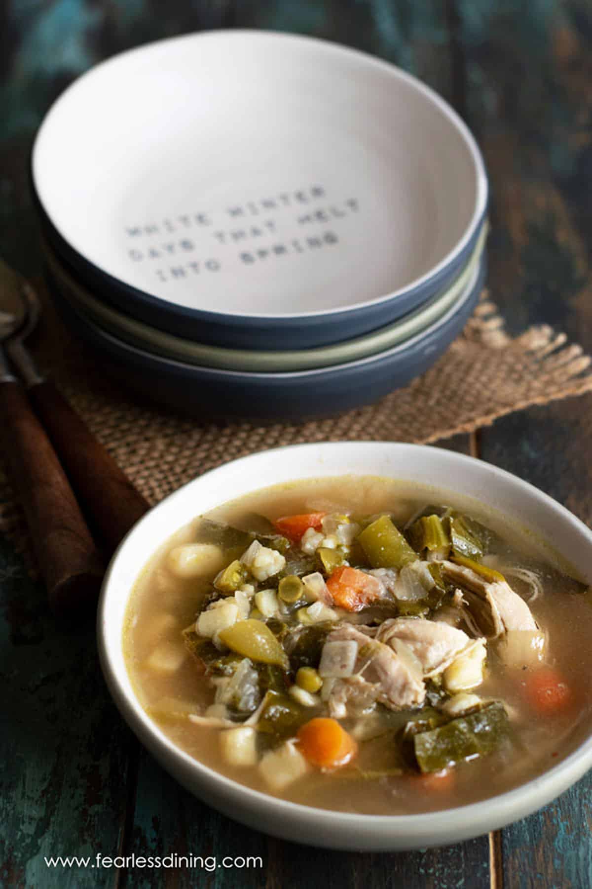 A soup bowl filled with bone broth vegetable soup. It is next to a stack of bowls.