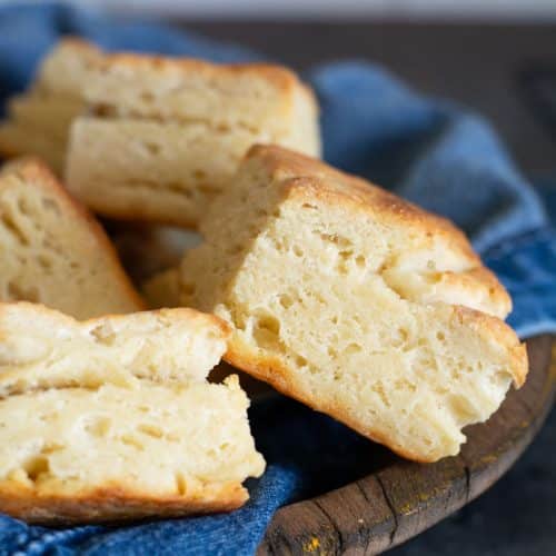 A wooden bowl with a denim napkin. The bowl is full of gluten-free sourdough discard biscuits.