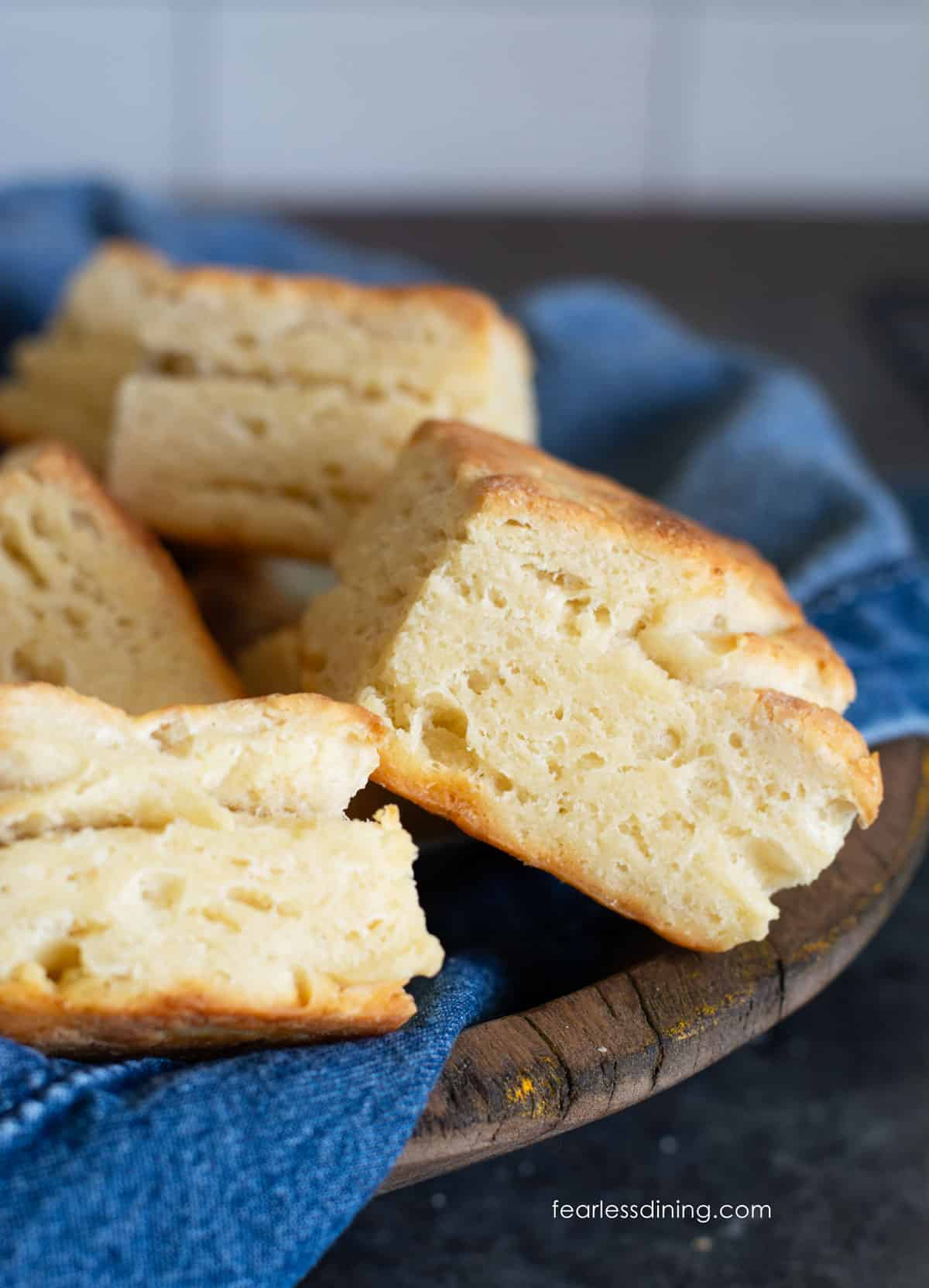 A wooden bowl with a denim napkin. The bowl is full of gluten-free sourdough discard biscuits.