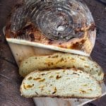 A loaf of cheddar sourdough on a cutting board next to two slices of the bread.