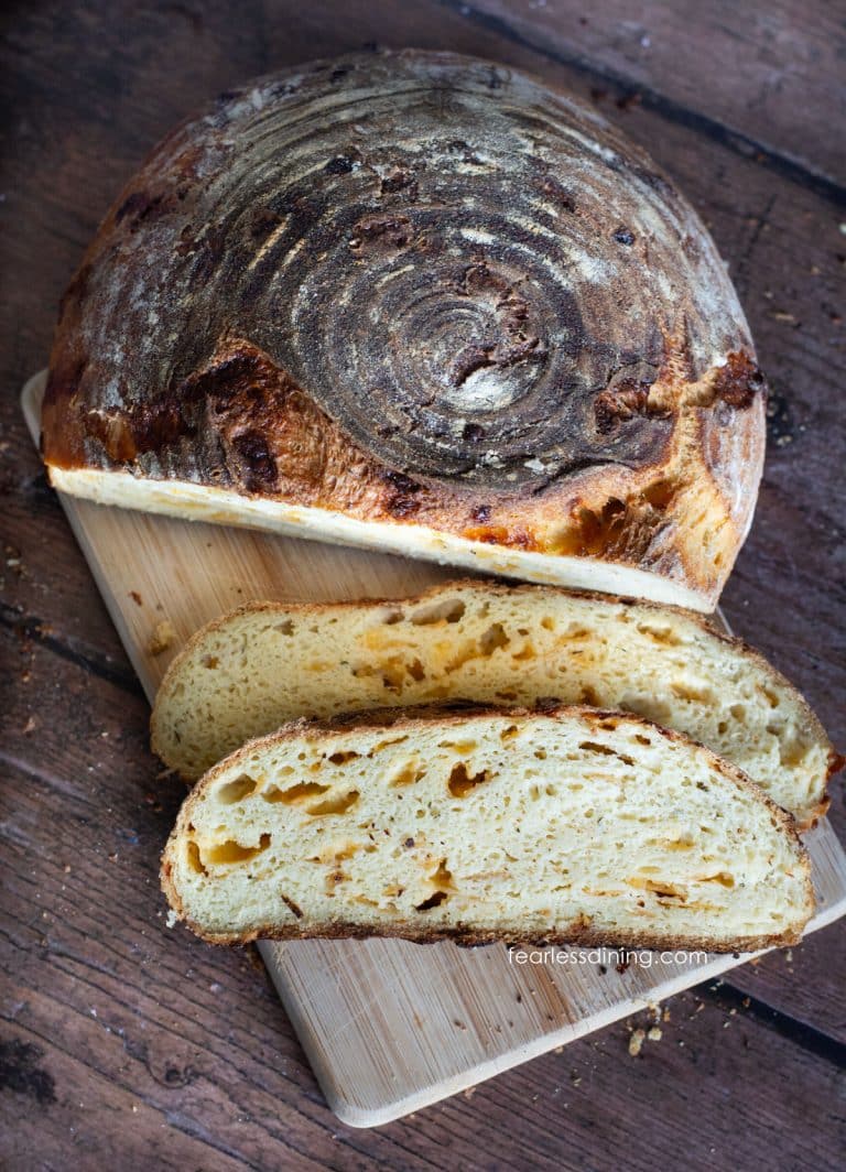A loaf of cheddar sourdough on a cutting board next to two slices of the bread.