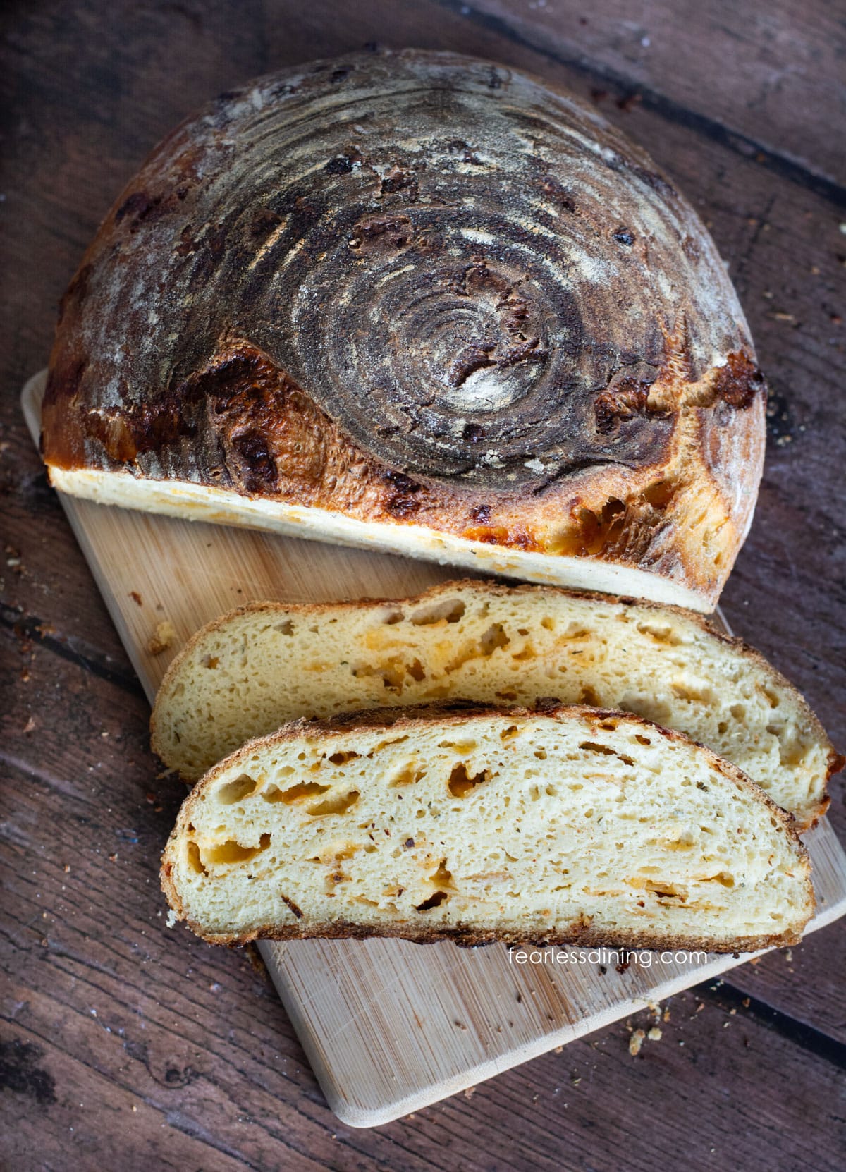 A loaf of cheddar sourdough on a cutting board next to two slices of the bread.