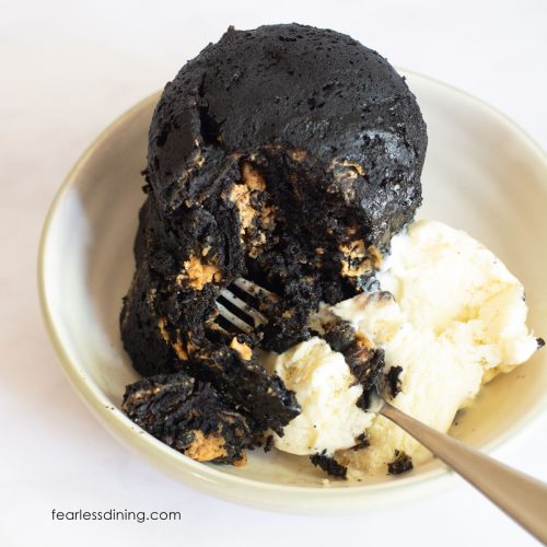 A gluten-free chocolate peanut butter mug cake with a scoop of vanilla ice cream and a fork cutting in.