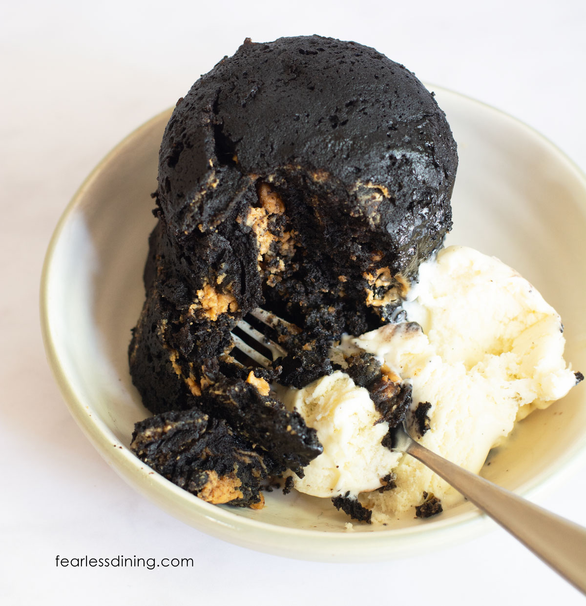 A gluten-free chocolate peanut butter mug cake with a scoop of vanilla ice cream and a fork cutting in.