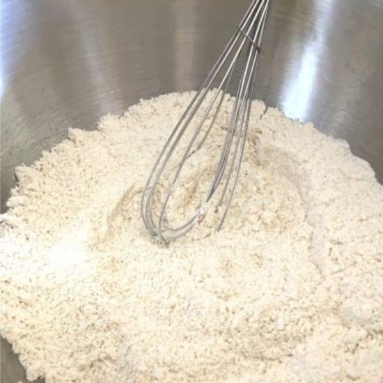 Using a whisk to mix the dry ingredients in the mixing bowl.