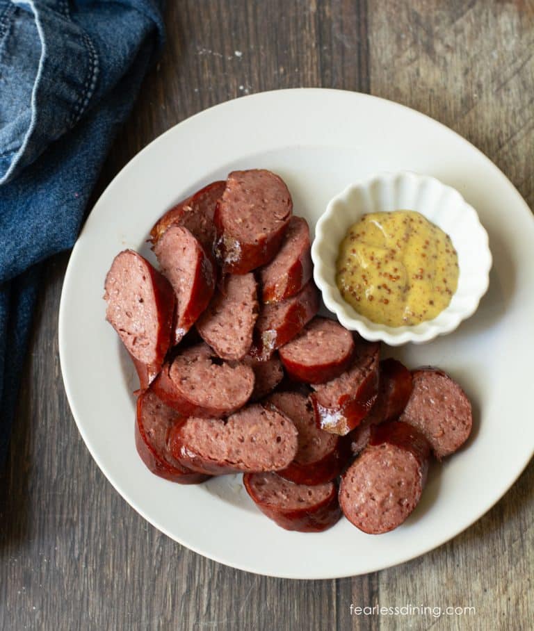 Sliced air fryer kielbasa on a large plate with a small dish of stone ground mustard for dipping.